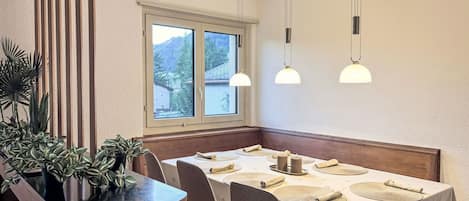 A dining area with a table set for four, a wooden bench, and a window with a view of a mountain.