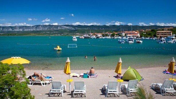 A beach with white lounge chairs and yellow umbrellas, a clear blue sea, and boats in the background. - Große Wohnung in Klimno mit Möbliertem Balkon by Interhome (Krk/Čižići)