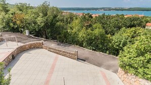 A paved area with a stone wall and metal railing, surrounded by dense green trees and a view of a coastal town. - Große Wohnung in Klimno mit Möbliertem Balkon by Interhome (Krk/Čižići)