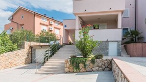 A modern apartment building with a stone staircase leading to a flat entrance, surrounded by greenery and a clear sky. - Große Wohnung in Klimno mit Möbliertem Balkon by Interhome (Krk/Čižići)