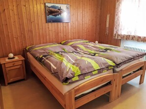 Un letto di legno con una coperta a motivi, un comodino con un oggetto sferico e un quadro appeso al muro.
