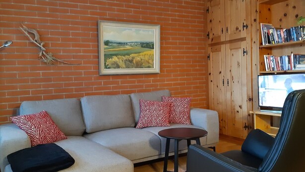 A living room with a sofa, a small round table, a black chair, a bookshelf, and a painting on the wall. - Chesa Suot Rövens by Interhome (Samedan)