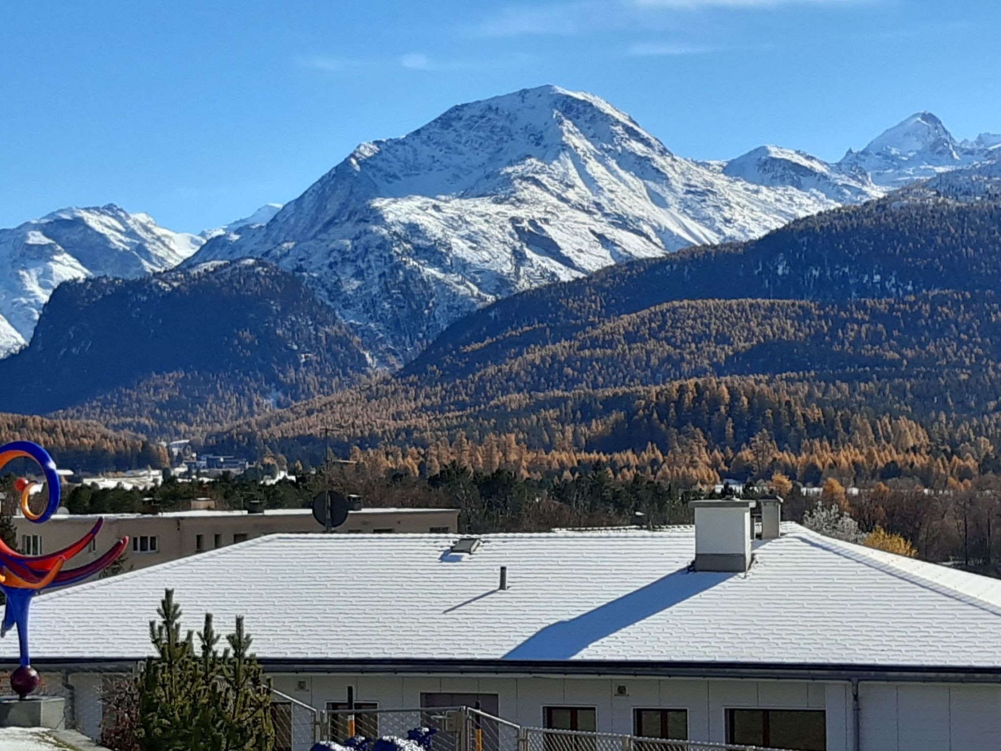 Un bâtiment doté d’un toit plat, entouré de montagnes enneigées et d’une zone boisée.