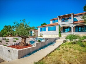 Ein zweistöckiges Haus mit Pool, einem Baum im Garten und blauem Himmel.