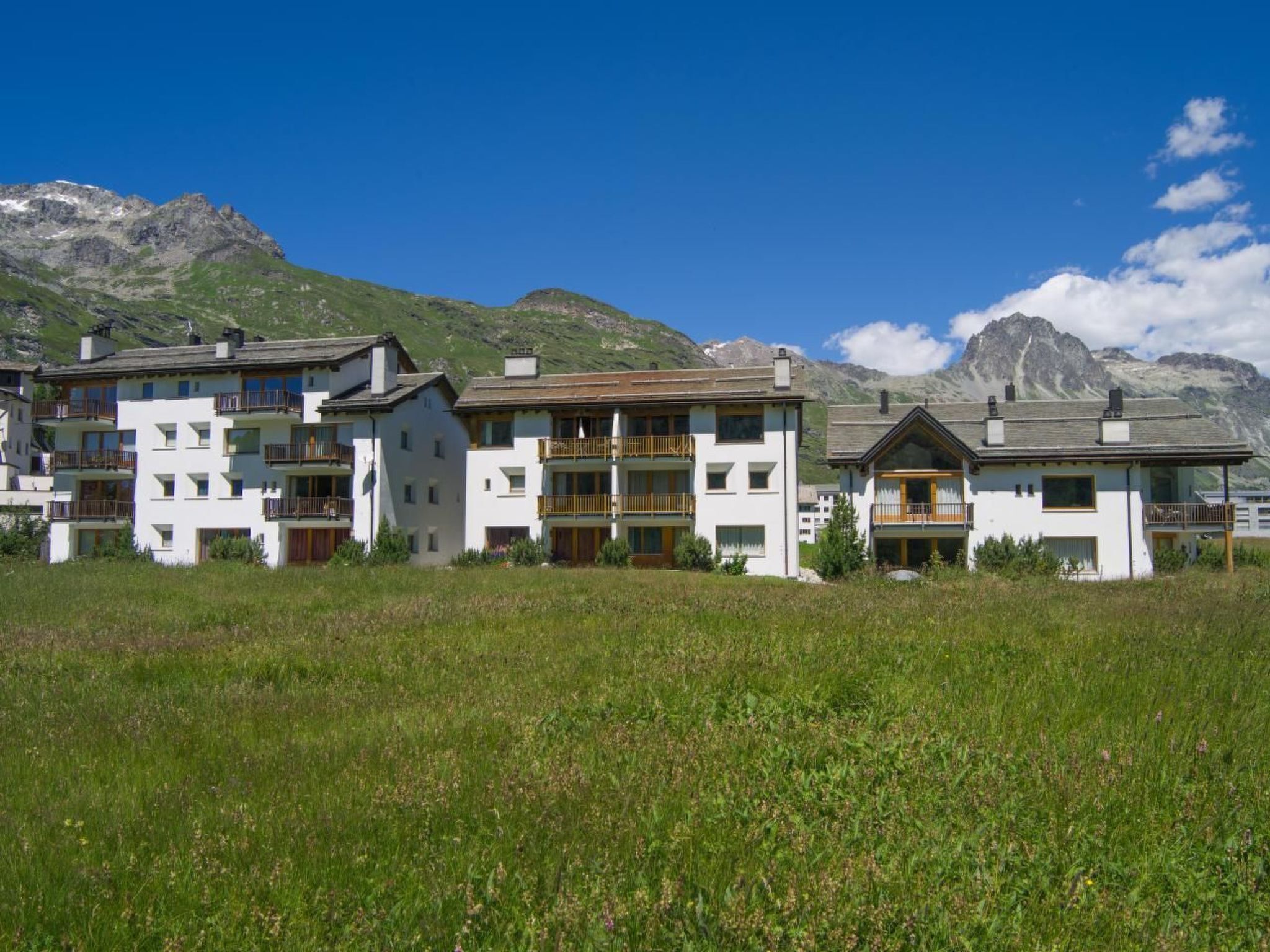 A row of white buildings with balconies, set against a mountainous backdrop.