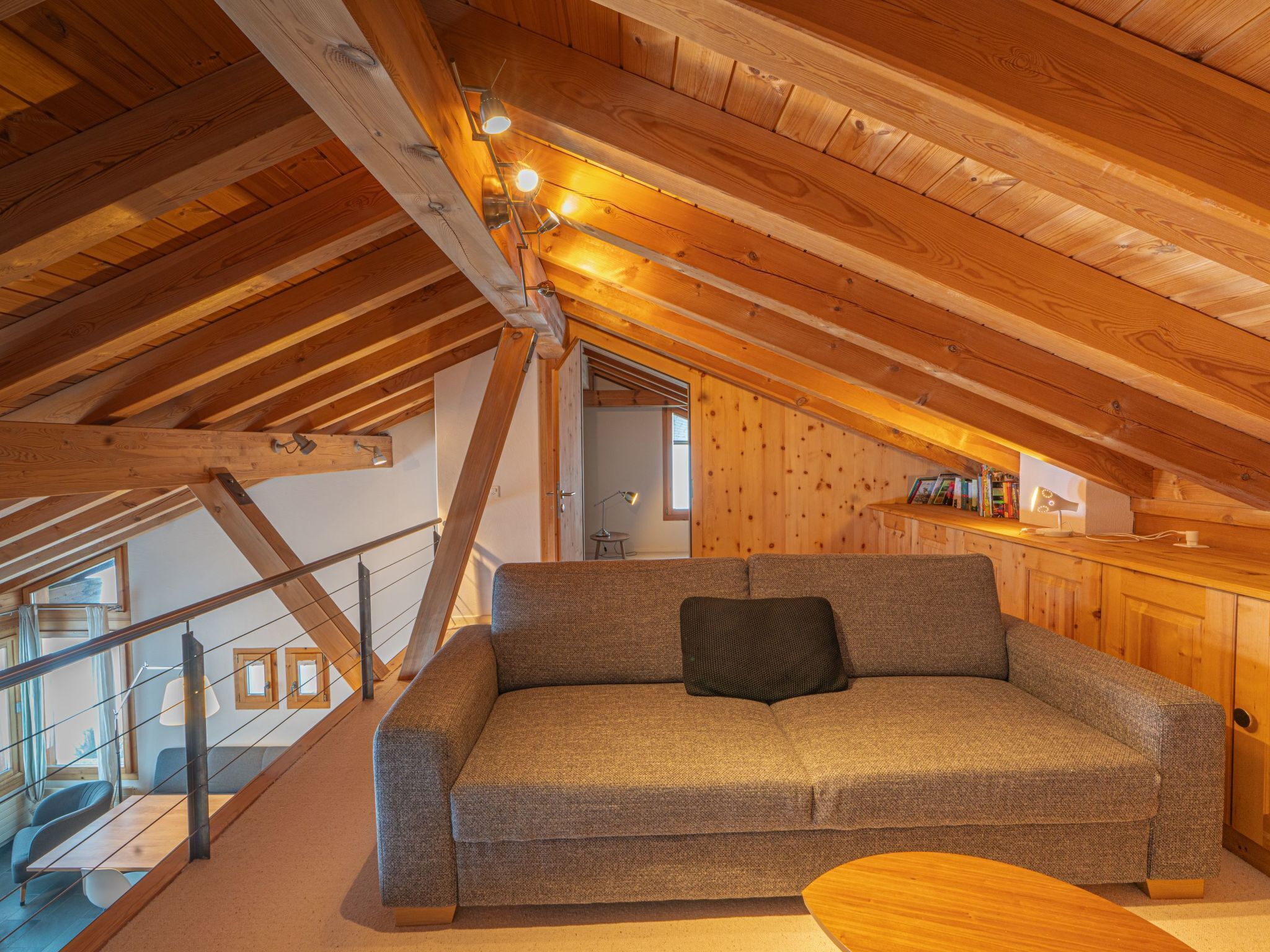 Una habitación acogedora en el ático con techo de madera, un sofá gris y una mesa de centro de madera.