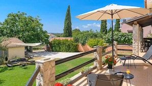 A patio with outdoor furniture, a table with a drink, and a view of a garden and a tall tree. - Komfortable, ruhige Erdgeschoss-Ferienwohnung by Interhome (Barban)