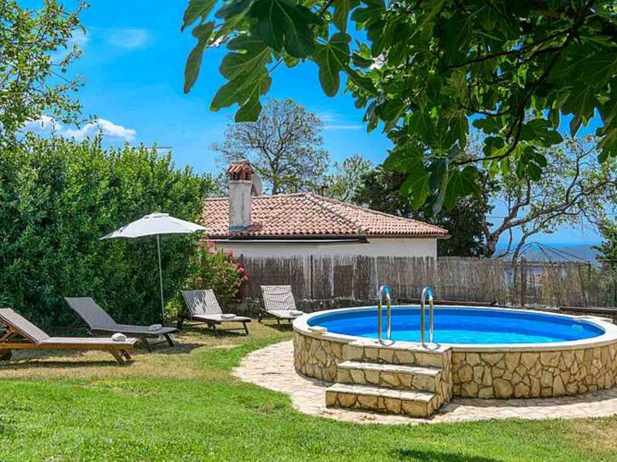 A backyard with a swimming pool, lounge chairs, and a view of the sea.