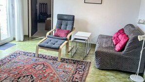Ein Wohnzimmer mit grauem Sessel, grauem Sofa, einem gemusterten Teppich, einem gerahmten Kunstwerk und einer Stehlampe.