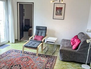 Ein Wohnzimmer mit grauem Sessel, grauem Sofa, einem gemusterten Teppich, einem gerahmten Kunstwerk und einer Stehlampe.