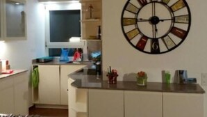 Una cocina con armarios blancos, un reloj de pared grande y diversos utensilios sobre la encimera.