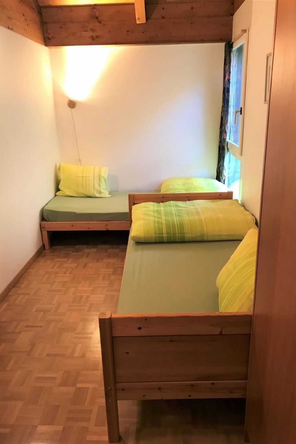Een kleine kamer met twee houten bedden, elk met een groene matras en gele kussens.