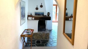 Un intérieur chaleureux avec une cheminée en pierre, une étagère en bois ornée d’objets décoratifs et un miroir encadré.