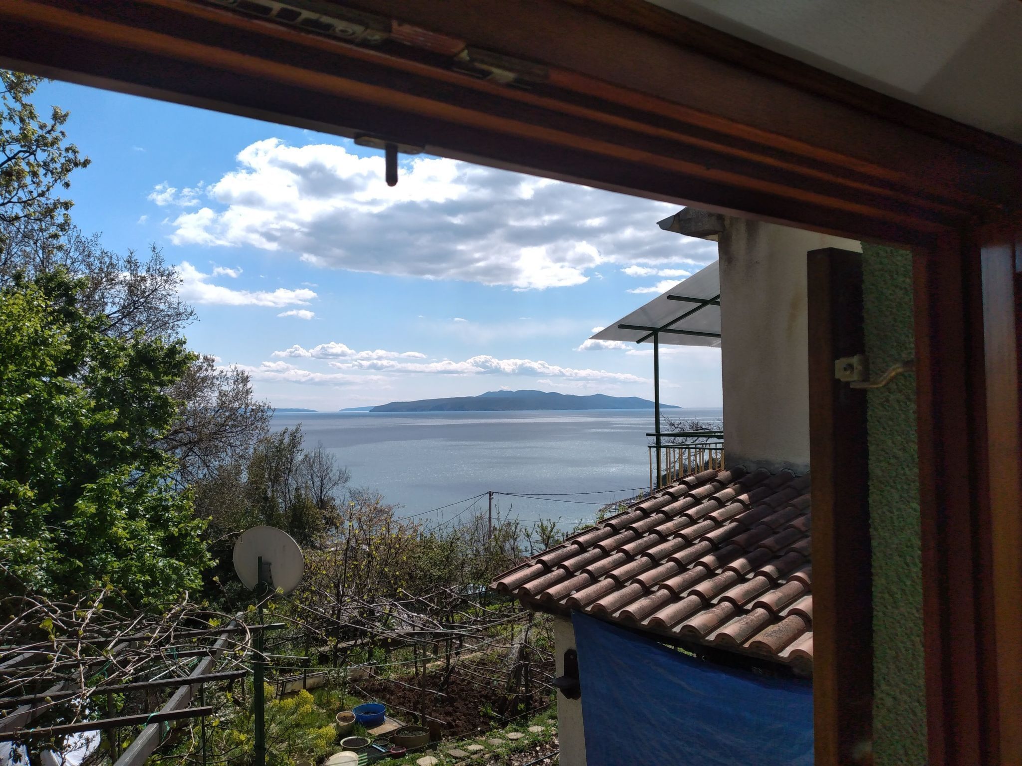 Blick vom Balkon auf ein Gewässer mit fernen Bergen, einer Satellitenschüssel und einem Ziegeldach.