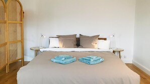 A neatly made bed with a beige bedspread, two bedside tables with lamps, and a woven headboard. - What a view by Interhome (Orselina)