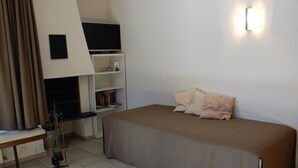 Ein Schlafzimmer mit Bett, Schreibtisch, Stuhl, Bücherregal und einem an der Wand befestigten Fernseher.