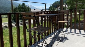 Ein Balkon mit Holzmöbeln und Metallgeländer mit Blick auf eine Berglandschaft.