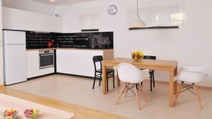 A modern kitchen with white cabinets, a black countertop, and a wooden dining table with four chairs. There is a clock on the wall and a fruit bowl on the table. - Wohnung mit Blick auf das Wasser by Interhome (Medulin/Ližnjan)