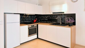 A modern kitchen with white cabinets, a black backsplash, a stainless steel refrigerator, an oven, a sink, and a clock on the wall. - Wohnung mit Blick auf das Wasser by Interhome (Medulin/Ližnjan)