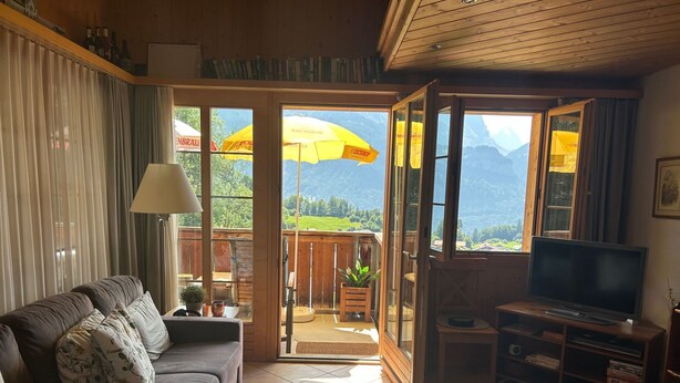 Una sala de estar acogedora con un sofá, un televisor y un balcón con un paraguas amarillo.