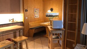 Interior de madera con área de cocina, una banca, un microondas y un reloj en la pared.