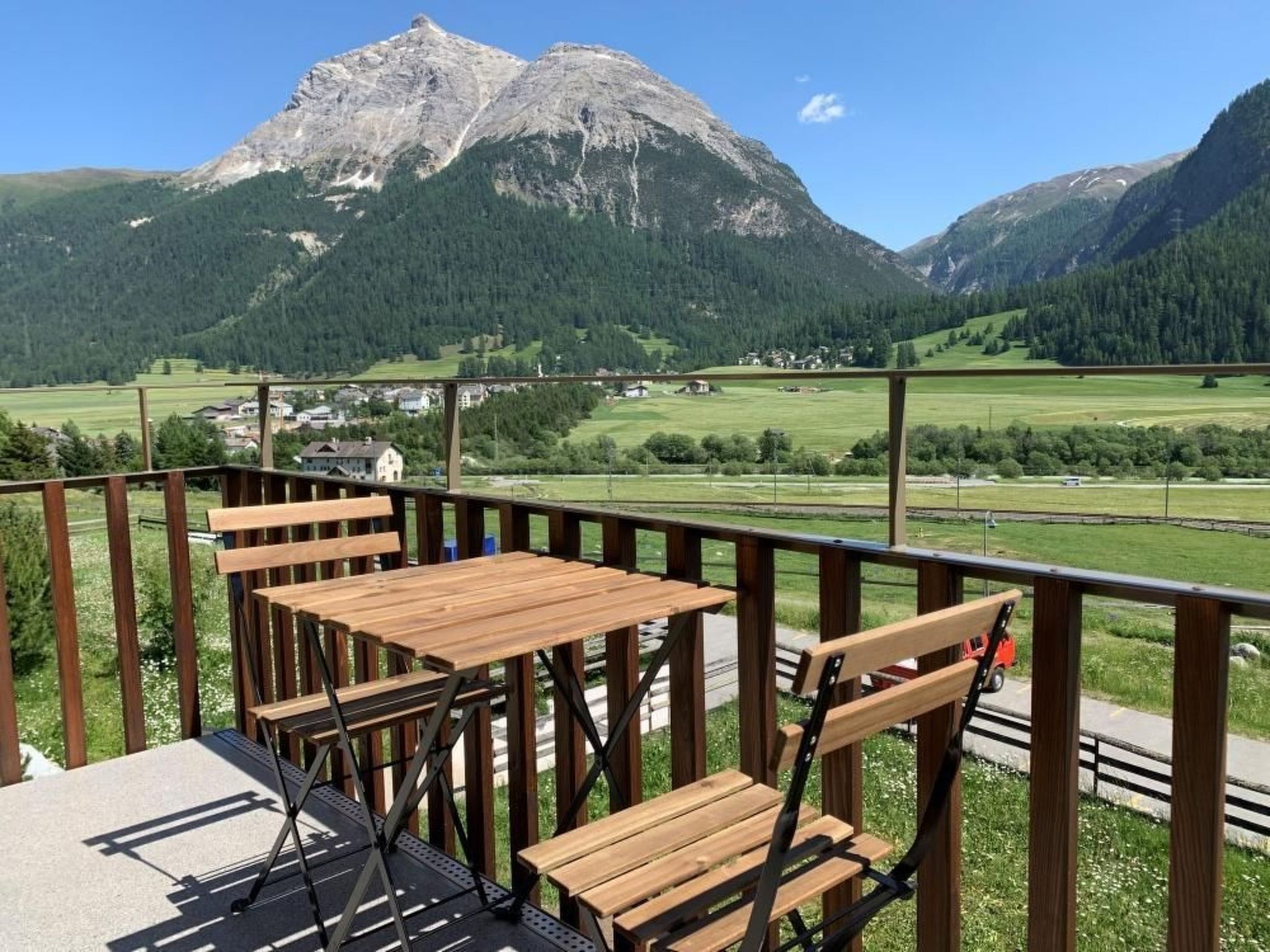 Terraza de madera con mesas y sillas, con vistas a un paisaje montañoso.