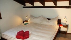 Una cama bien tendida con sábanas blancas y toallas rojas, dos lámparas de noche y un cabecero de madera.