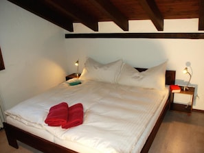 Ein ordentlich bezogenes Bett mit weißen Laken und roten Handtüchern, zwei Nachttischlampen und ein Holz-Kopfteil.