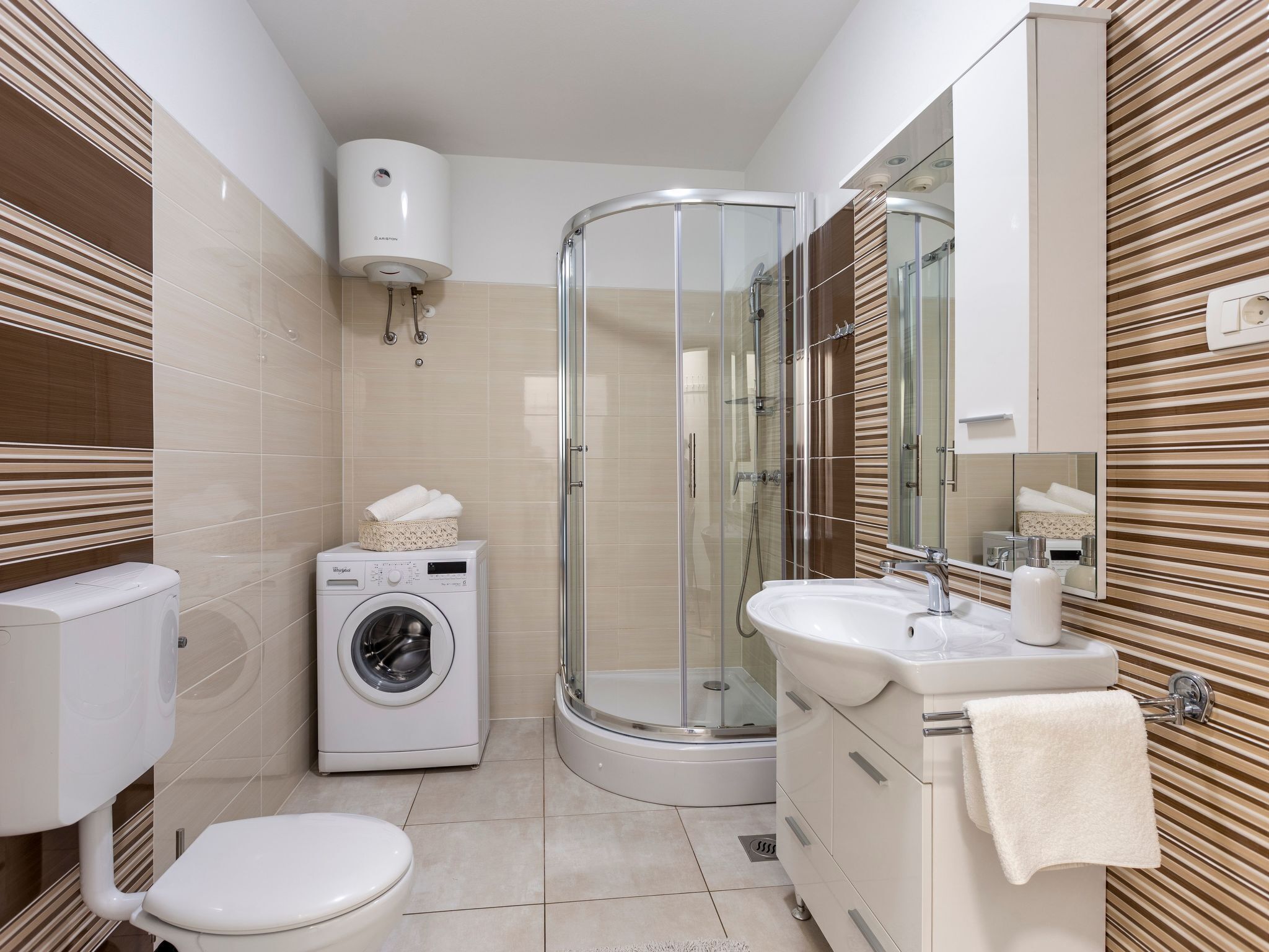 Un bagno moderno con doccia vetrata, lavatrice, WC e lavandino con un asciugamano appeso al muro.