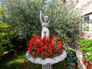 A statue of a figure with raised arms, surrounded by a planter with red flowers. - Apartment  by Interhome (Poreč/Funtana)