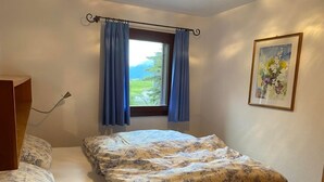 Un dormitorio con cama, ventana con cortinas, un cuadro en la pared y cabecero de madera.