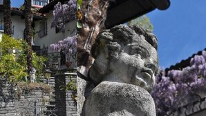 A stone statue with a rough texture, set against a backdrop of a building with purple flowering vines and a clear blue sky. - Studio Cresta Bianca by Interhome (Ronco sopra Ascona)