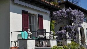 A building with a white facade, red shutters, and a balcony with statues. - Studio Cresta Bianca by Interhome (Ronco sopra Ascona)