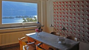 Uma área de refeições com vista para um lago, uma mesa com cadeiras, um vaso com flores e uma parede estampada.