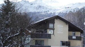 Een gebouw met twee verdiepingen en een balkon, omgeven door met sneeuw bedekte bomen en bergen op de achtergrond.