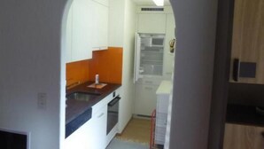 Een smalle keuken met witte kastjes, een donker aanrecht en een houten deur.