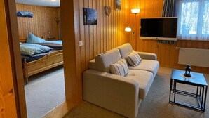 A cozy room with a wooden interior, a sofa, a TV, and a bed with pillows. - Chalet am Bühl by Interhome (Grindelwald)