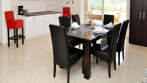 Uma cozinha moderna com armários brancos, uma mesa de jantar posta para seis com cadeiras pretas, e vista para o exterior através de uma grande janela.