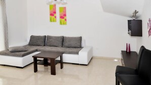 Uma sala de estar moderna com um sofá modular branco, uma mesa de centro em madeira escura e uma poltrona de couro preto. Há duas pinturas abstratas na parede e um armário de madeira escura com um vaso em cima.