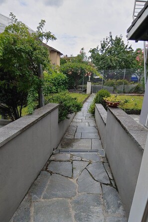 A stone pathway leading to a gate, surrounded by greenery and a fence. - Il Baitone 1 by Interhome (Minusio)