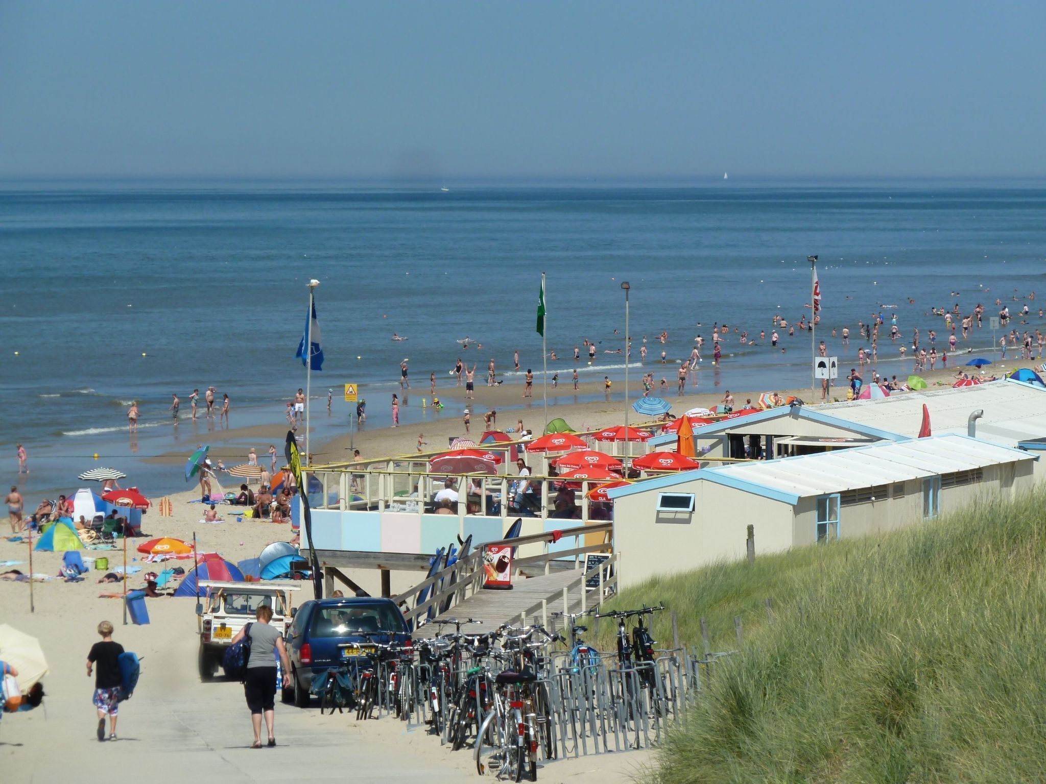 Une zone aménagée au bord de la plage, avec un parking, des vélos et des parasols de plage.