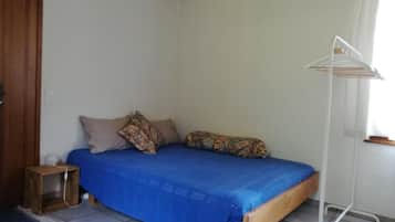 Une chambre avec un lit simple, une tête de lit en bois, une petite table de chevet et un étendoir blanc adossé au mur.