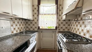 Uma cozinha compacta com armários brancos, fogão a gás, forno embutido e máquina de lavar louça.