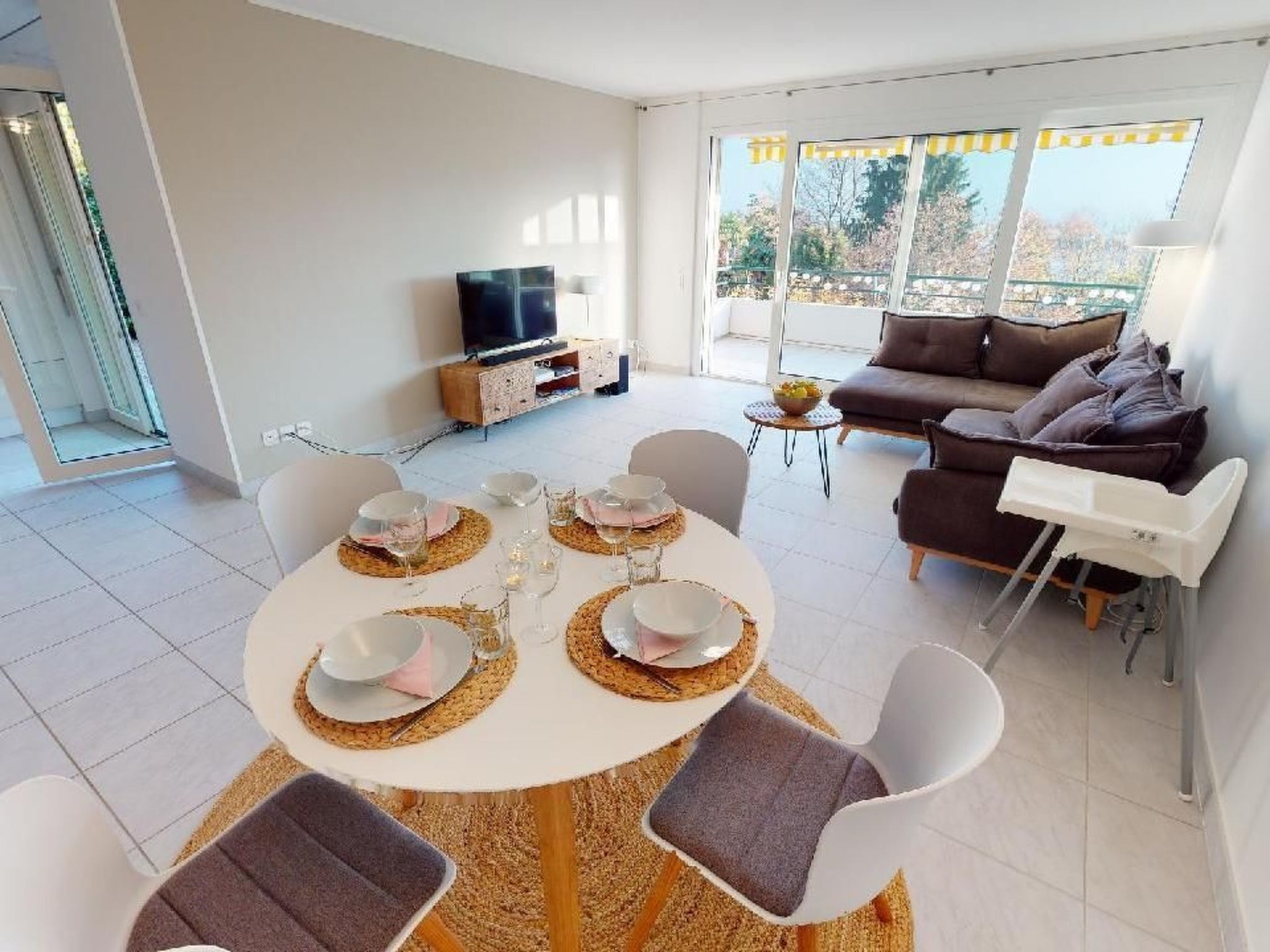 Un soggiorno moderno con zona pranzo per quattro persone, divano, televisione e balcone con vista.