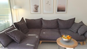 A modern living room with a grey sectional sofa, a small round table with a bowl of fruit, and three framed pictures on the wall. - Casa delle Vigne by Interhome (Minusio)