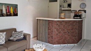 Un espace de vie moderne agrémenté d’un mur en briques apparentes, d’un canapé blanc, d’un coin café et d’un tableau représentant des voiliers.
