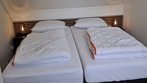 Une chambre double avec deux lits simples, chacun doté de draps blancs et d’une tête de lit en bois.