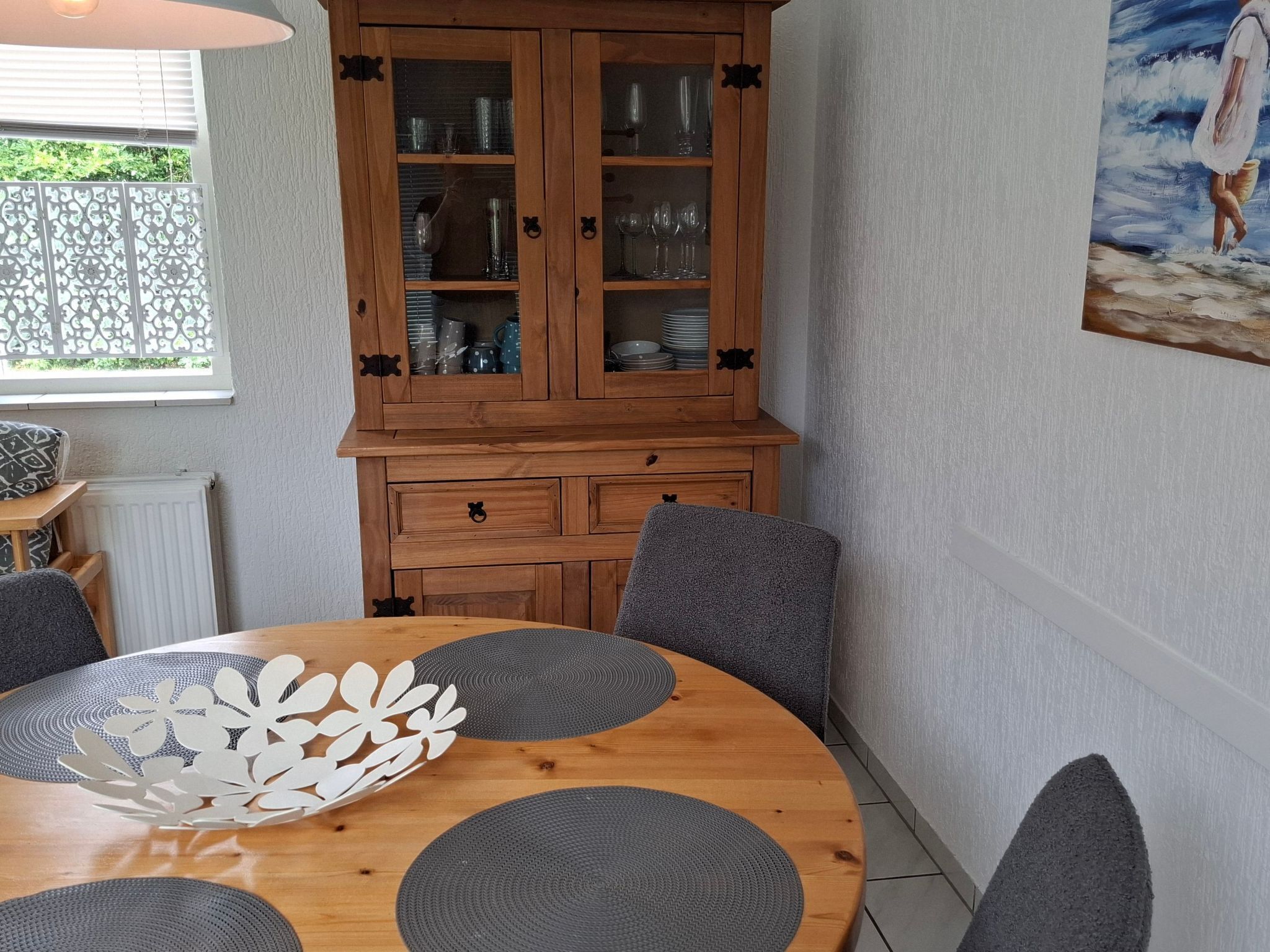 Un coin repas comprenant un buffet en bois, des chaises grises et une table ronde agrémentée d’un élément décoratif central.