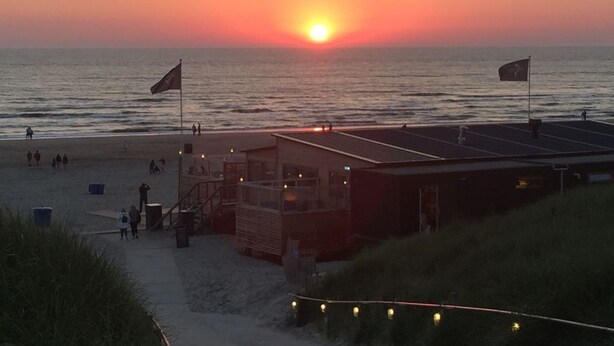 A beach scene with a sunset, a lifeguard tower, and a building with a roof. - De Blenck 66 by Interhome (Callantsoog)
