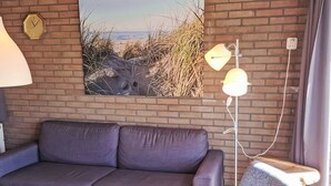 A modern living room with a brick wall, a sofa, a chair, a lamp, and a clock. - De Blenck 66 by Interhome (Callantsoog)